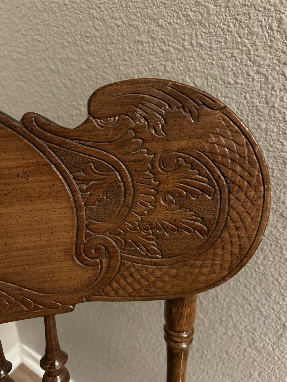 relief-carved detail of a dragon or seahorse-like creature in the head-rest board of the rocking chair.